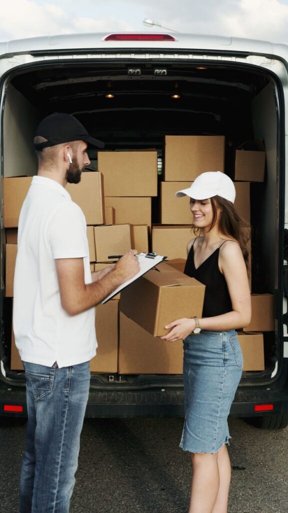 pexels photo 5025502 A delivery person hands a package to a woman from a van full of parcels outdoors.