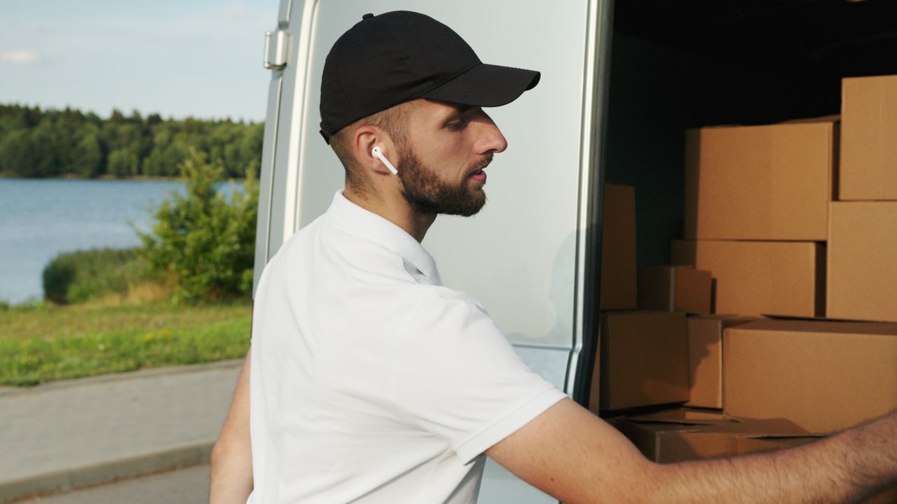 services-02 Courier wearing earphones loading packages into a van by a lakeside road.