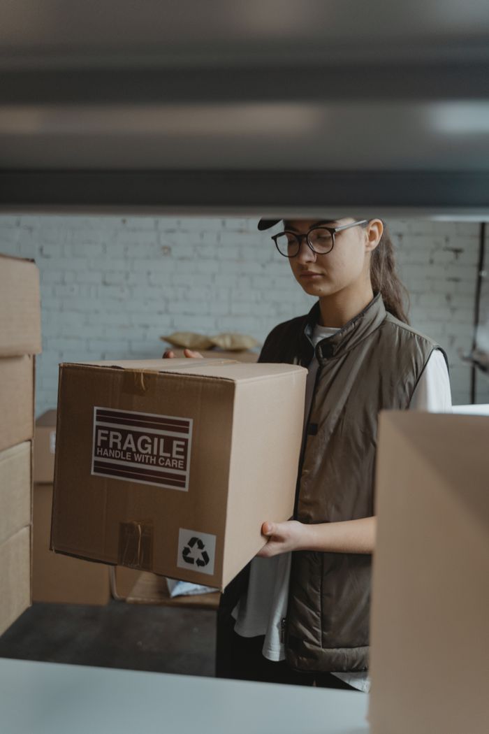why-choose-us Female courier handling a fragile package in a warehouse setting.
